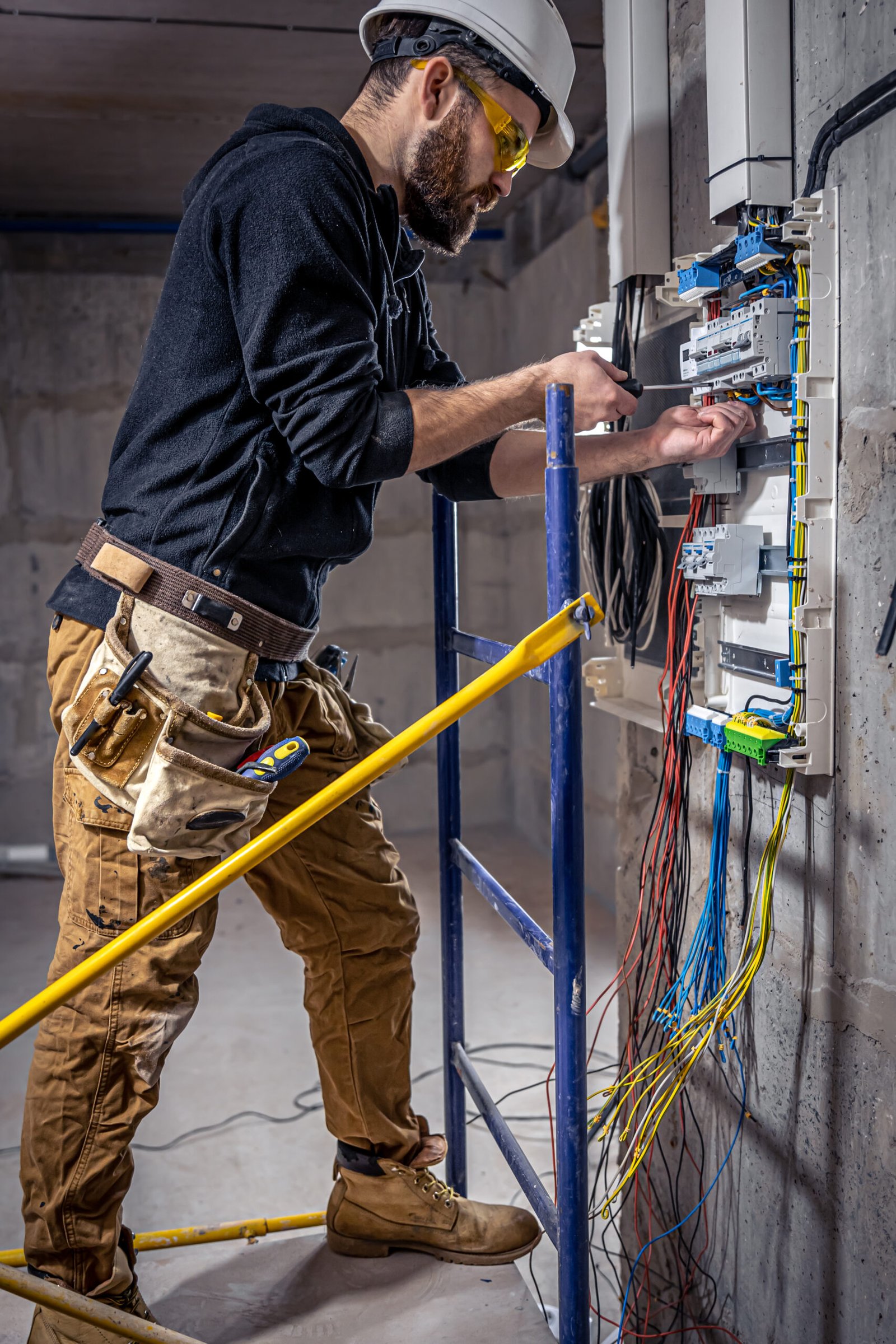 A male electrician works in a switchboard with an electrical connecting cable, connects the equipment with tools.